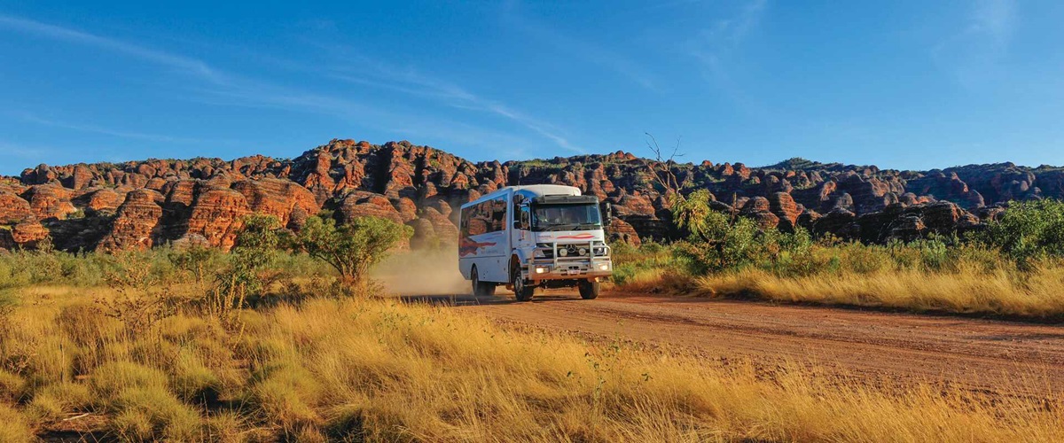 4WD coach travelling on a dirt road through with the Bungle Bungles in background