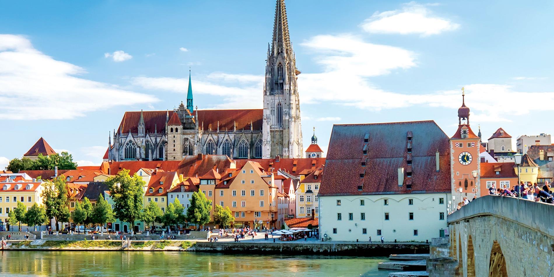 Historic old buildings and church along river with stone bridge in Regensburg, Germany