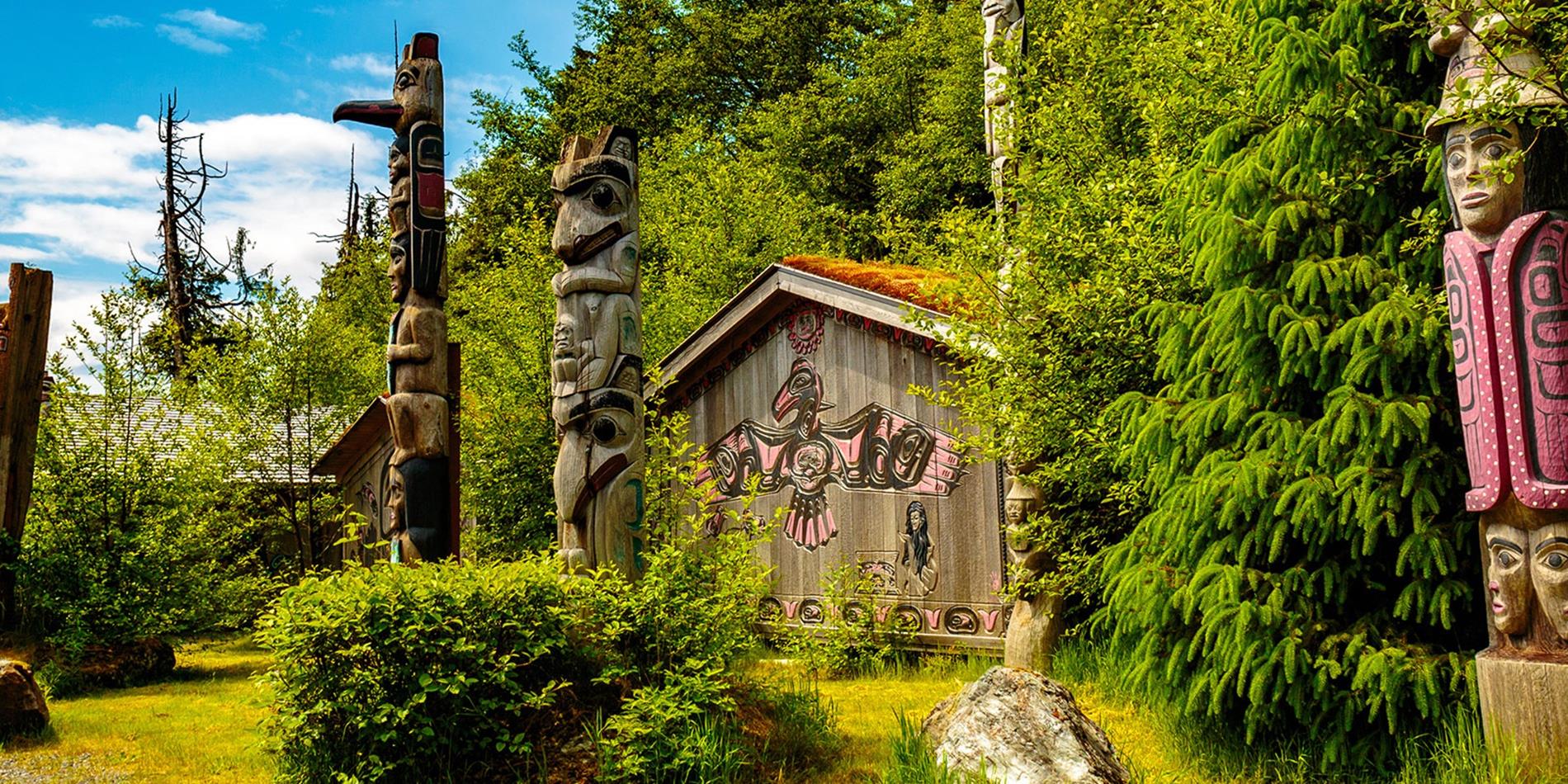 Wooden hand carved totem poles set amongst the trees and timber clad house